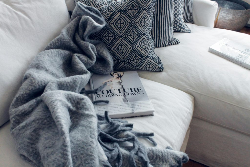 A modern living room with a white sofa, patterned pillows, and a cozy blanket.