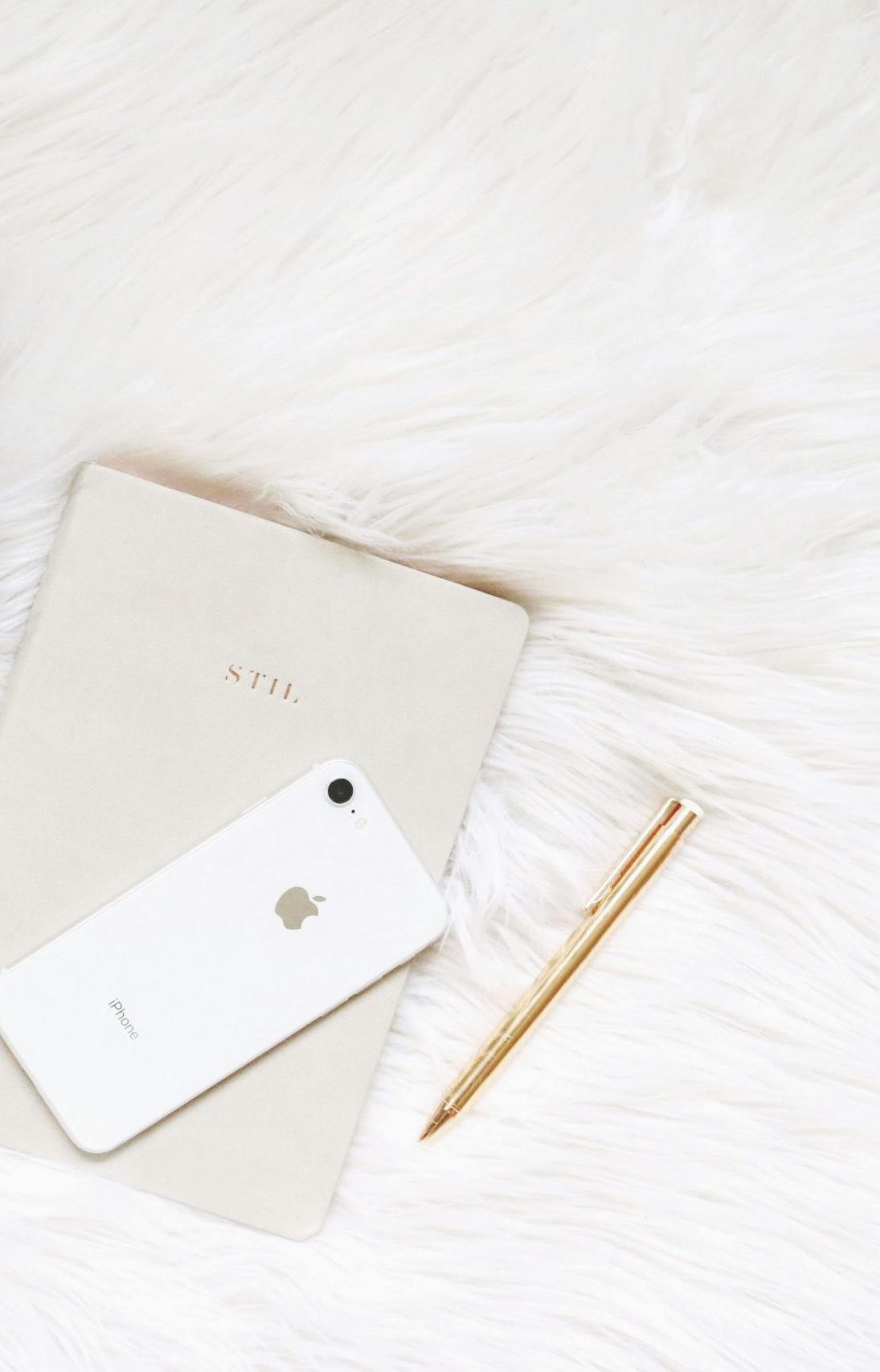 Minimalist flat lay of coffee, smartphone, notebook, and pen on white fur.